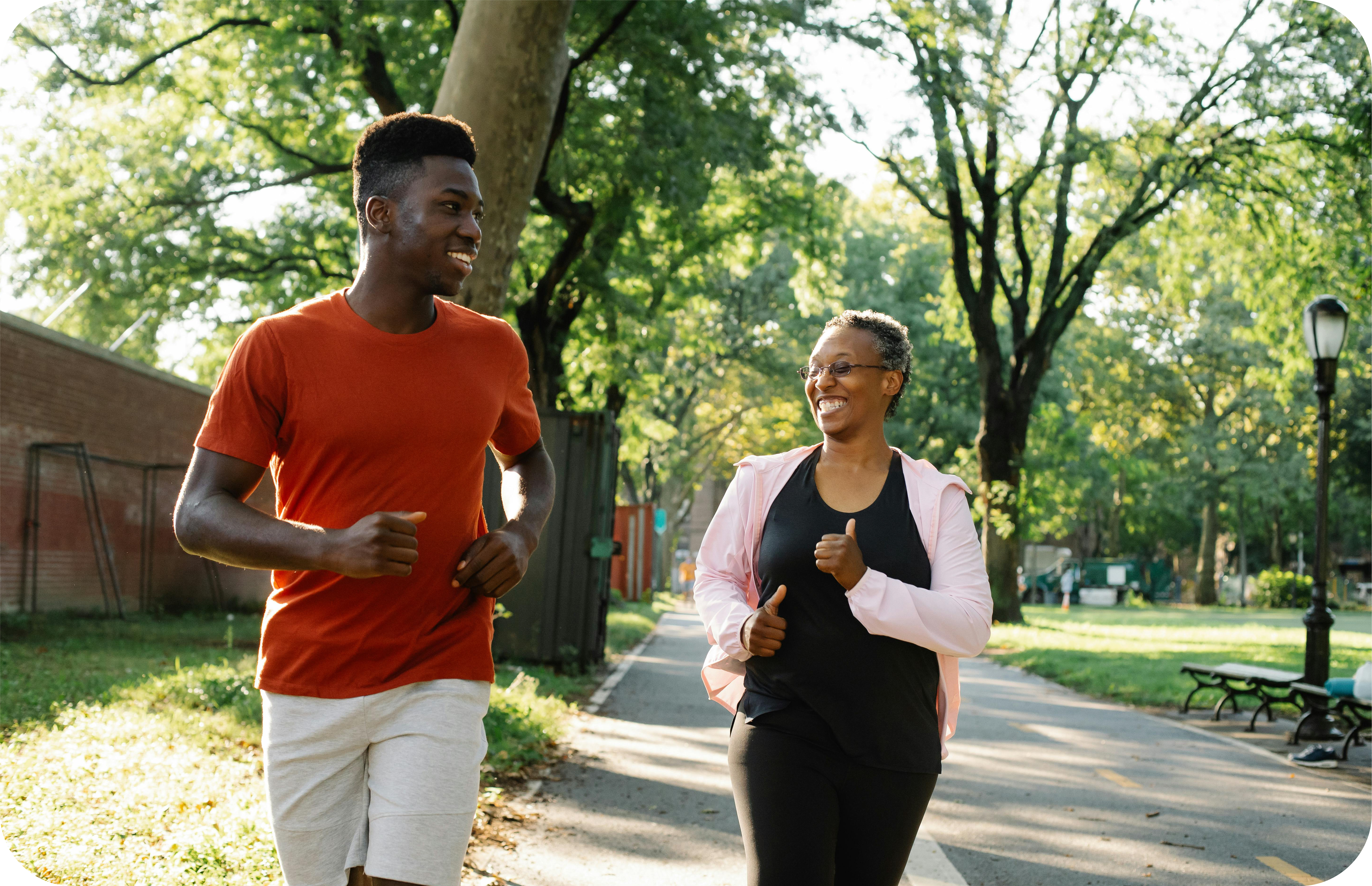 An image of an older Black woman and a young Black man smiling and jogging in an open park space.